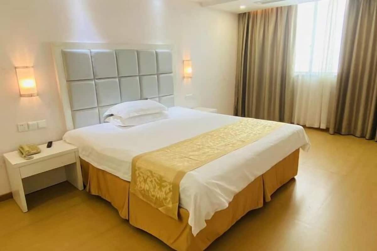 A hotel room with a large bed, a nightstand, a lamp, and a window with curtains.