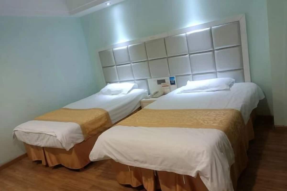 A room with two single beds, each with a wooden headboard and a white mattress cover.
