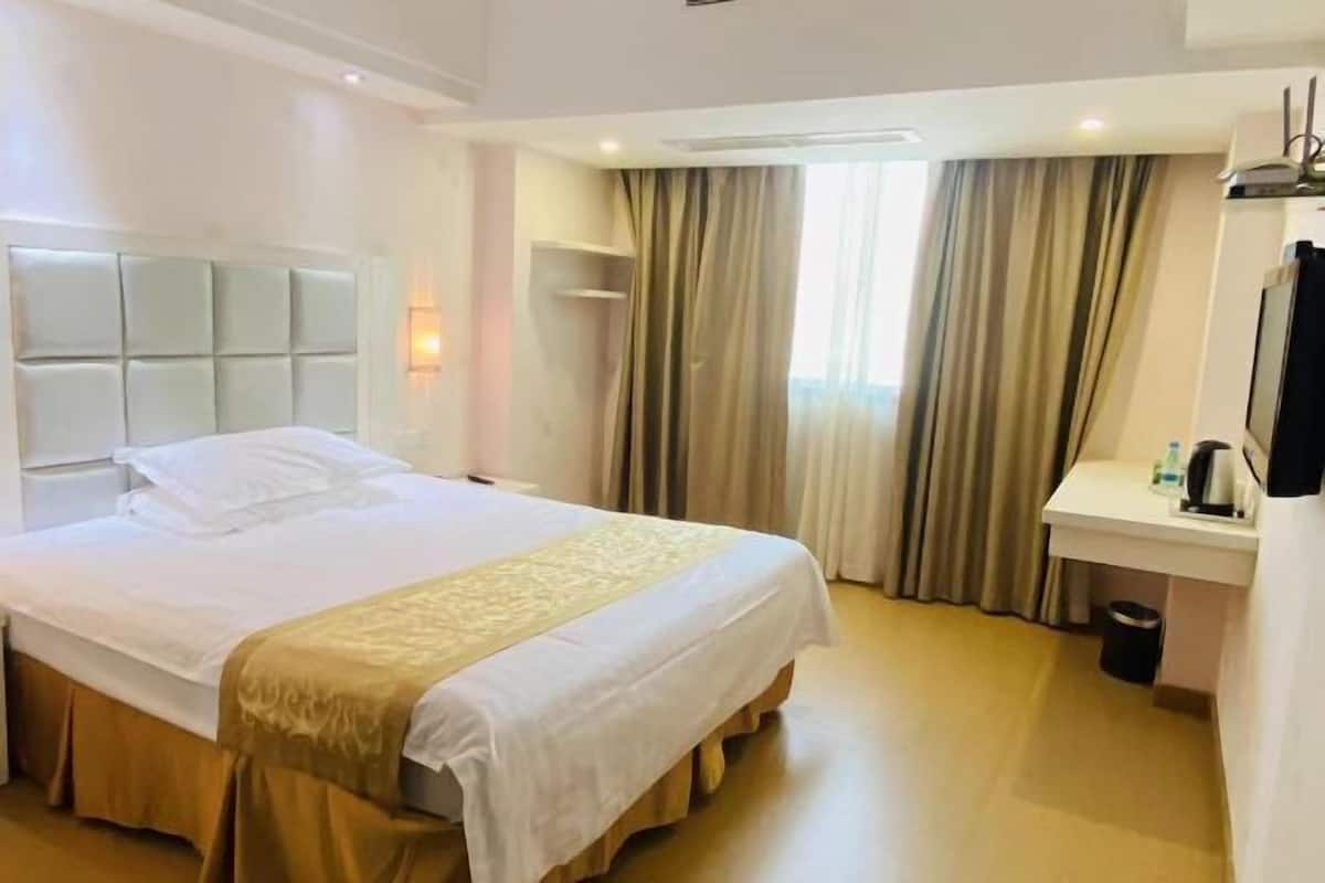 A hotel room with a bed, bedside table, and a small desk with a chair.