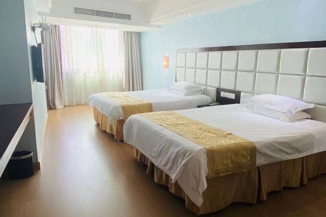 Una habitación de hotel con dos camas, un ventanal con cortinas, un televisor de pantalla plana y piso de madera.