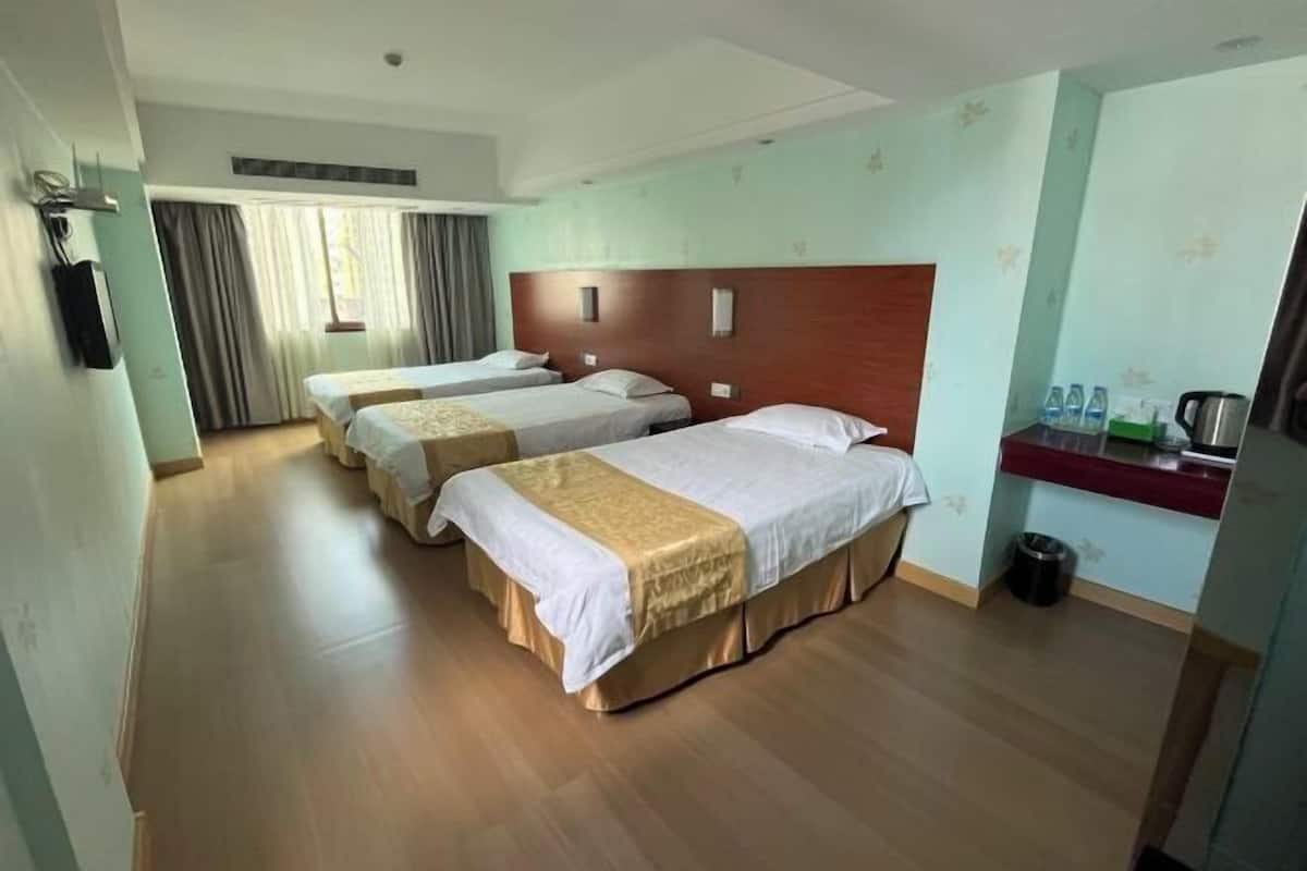 A hotel room with three beds, a wooden headboard, a small kitchen area, and a window with curtains.