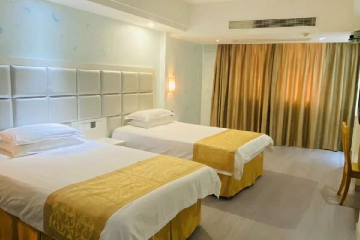 A hotel room with two beds, a headboard, a wall-mounted light, and a curtain.