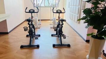 A hallway with two stationary bikes, a potted plant, and a window with blinds.