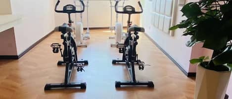 A hallway with two stationary bikes, a potted plant, and a window with blinds.