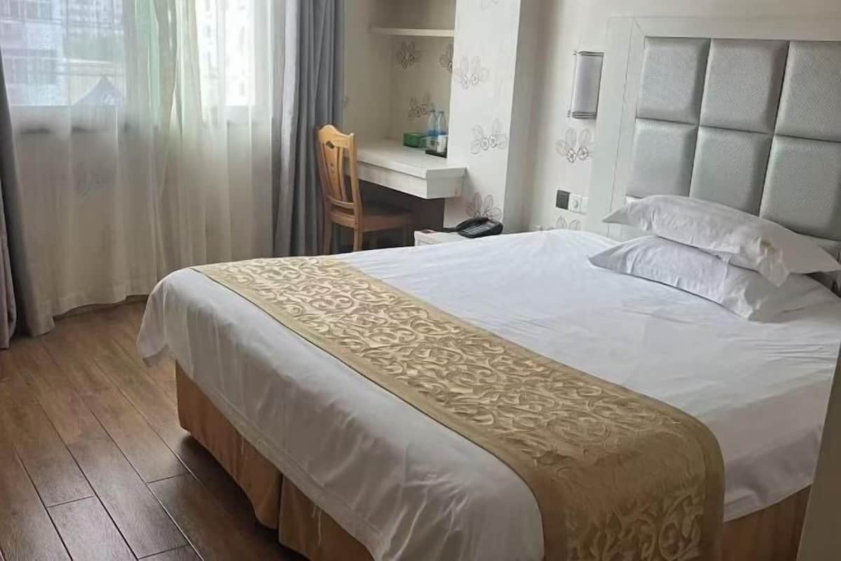 A hotel room with a large bed, a desk, and a chair.