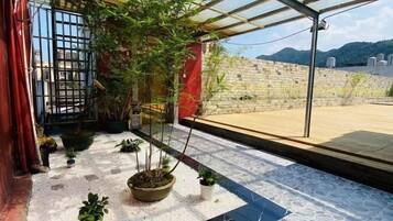 Terraço no telhado com plantas em vasos, estrutura de vidro e vista para uma parede de pedra e paisagem distante.