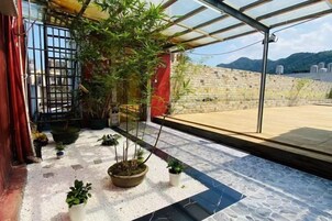 Terraza en la azotea con plantas en macetas, cerramiento de vidrio y vistas a un muro de piedra y paisaje lejano.