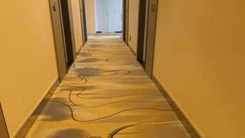 A hotel hallway with a patterned floor, doors on either side, and a light source at the end.