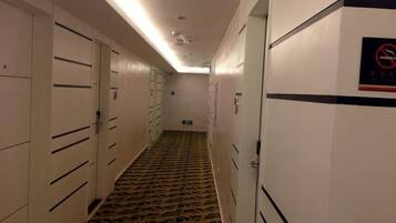 A hotel corridor with lockers, a patterned carpet, and a no-smoking sign.