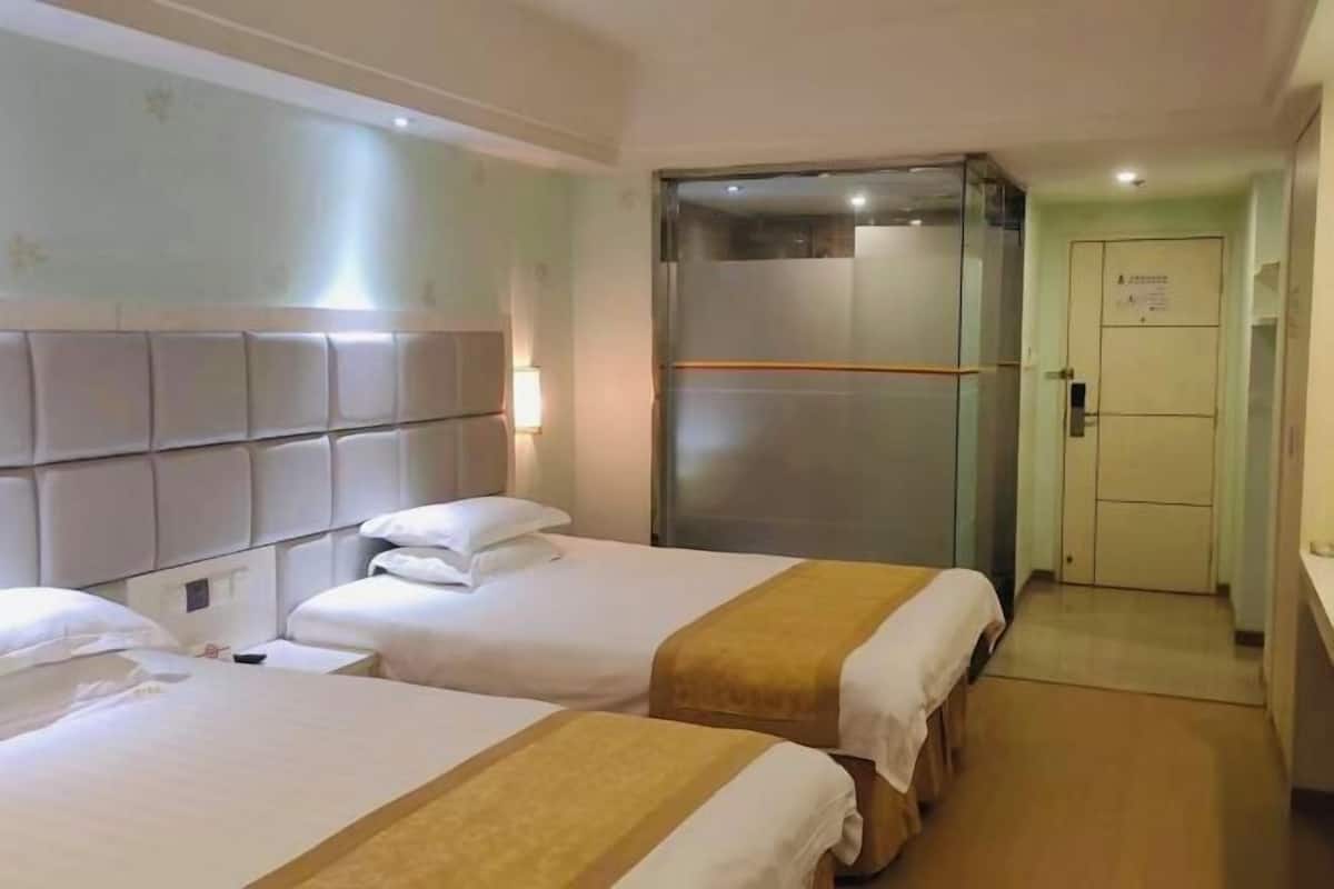 A hotel room with two beds, a minibar, a glass-enclosed shower, and a door with a sign.