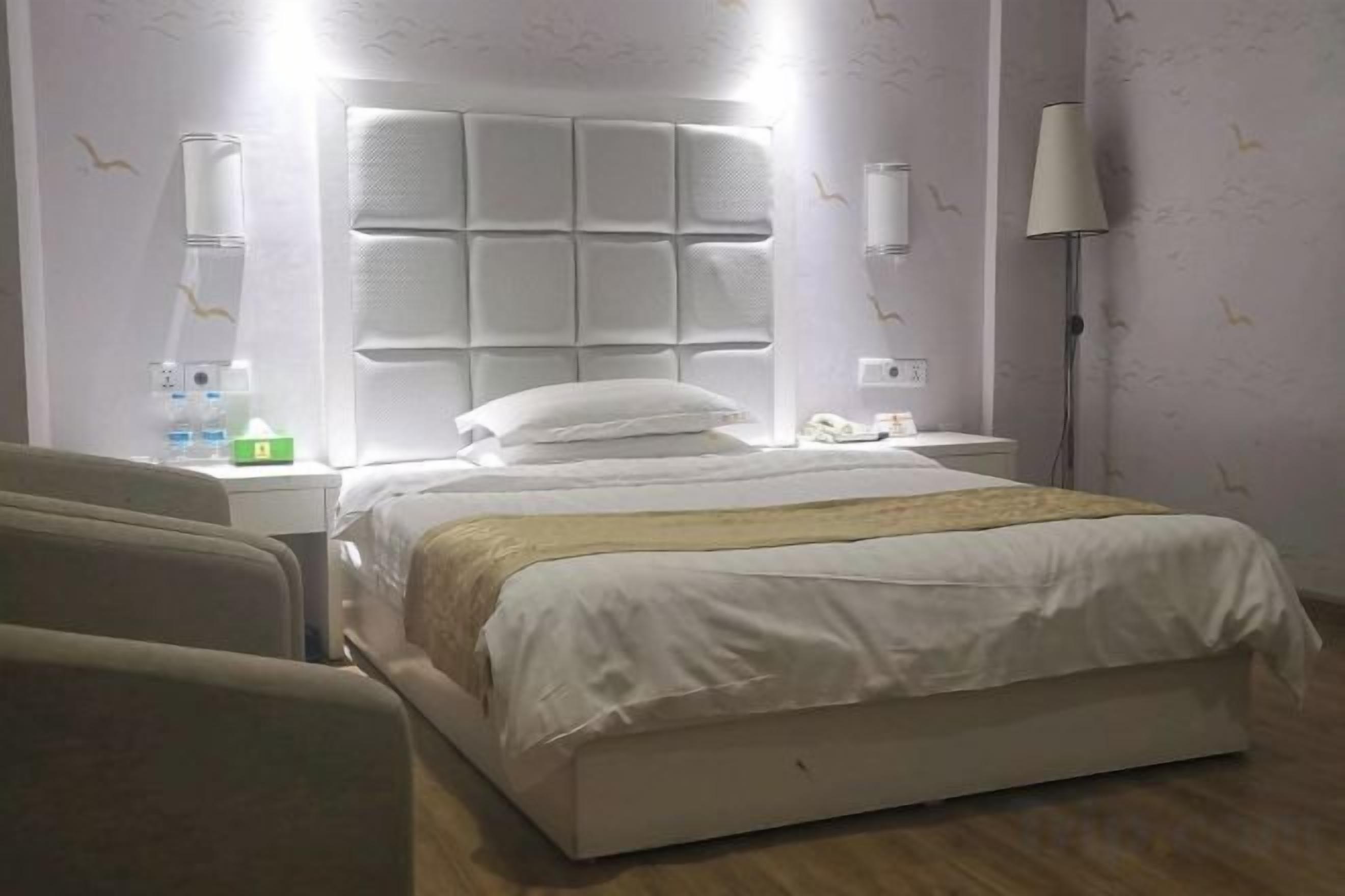 A hotel room with a large bed, a bedside table, a lamp, and a chair.