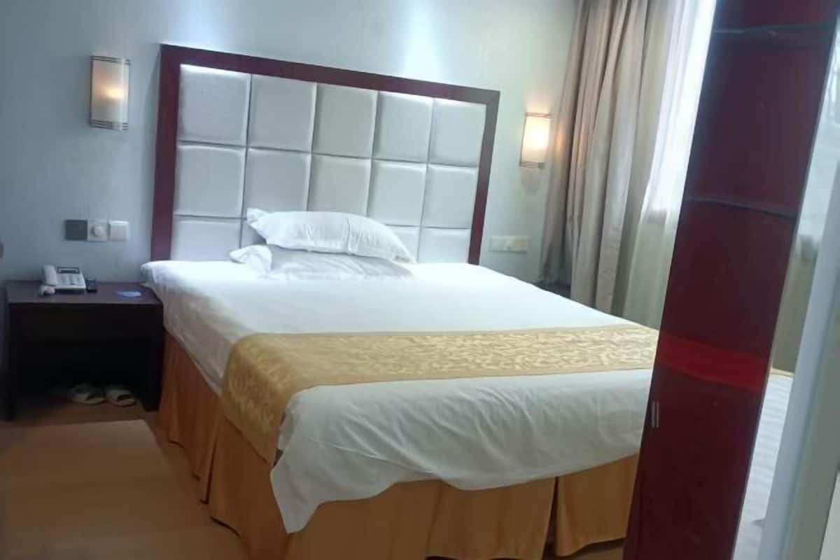 A hotel room with a large bed, a nightstand with a phone, and a wall-mounted light.