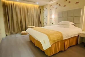 A hotel room with a large bed, a bedside table, a small stool, and a curtain.