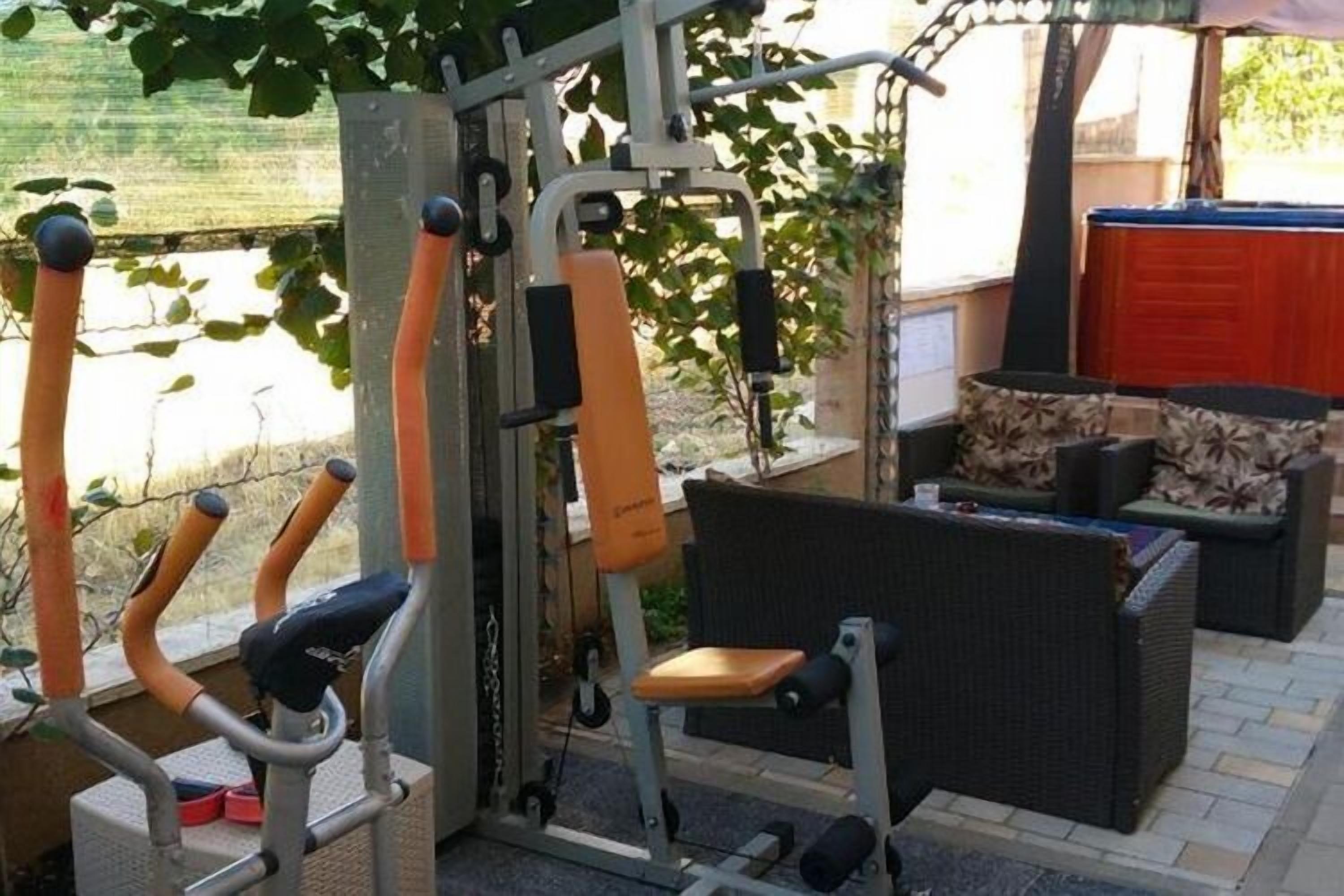An outdoor gym with exercise equipment, a wicker sofa, and a red door in the background.