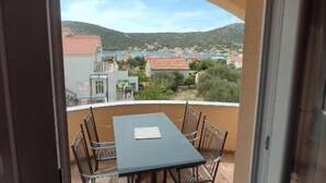 A balcony with a table and chairs, overlooking a coastal town with buildings and hills. - Apartments Vala - One Bedroom Apartment with Balcony and Sea View A4 (Vinisce)