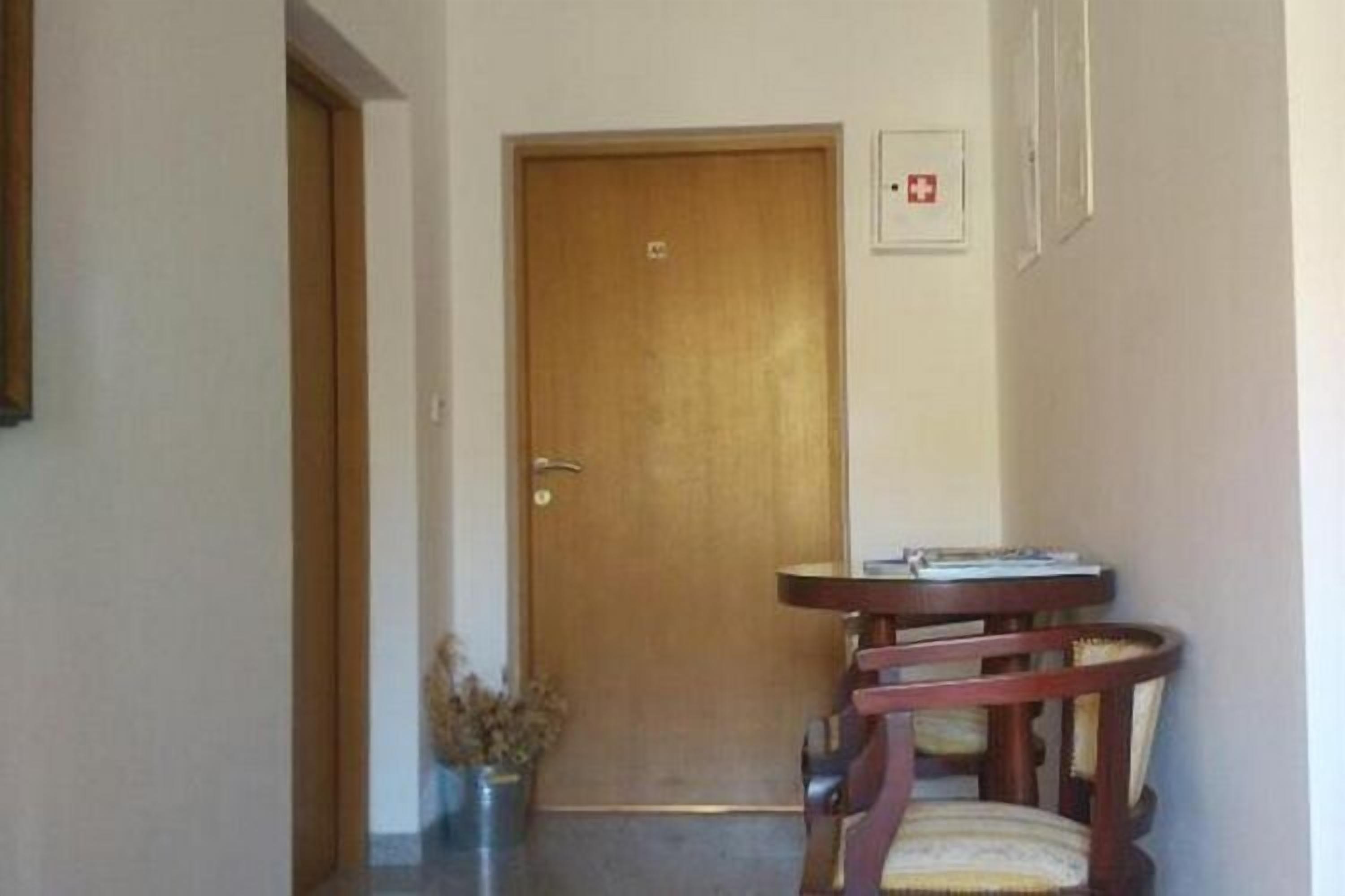 A hallway with a wooden door, a small table with chairs, and a framed emergency exit sign on the wall.