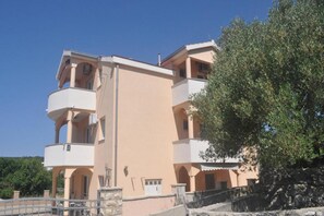 Un immeuble à plusieurs étages doté de balcons, d’un mur en pierre et d’un arbre.