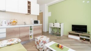 A modern living room with a flat-screen TV, a sofa, a coffee table, and a kitchen area with a microwave and cabinets.