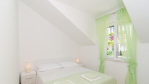 A bedroom with a single bed, a nightstand with a lamp, and a window with green curtains.