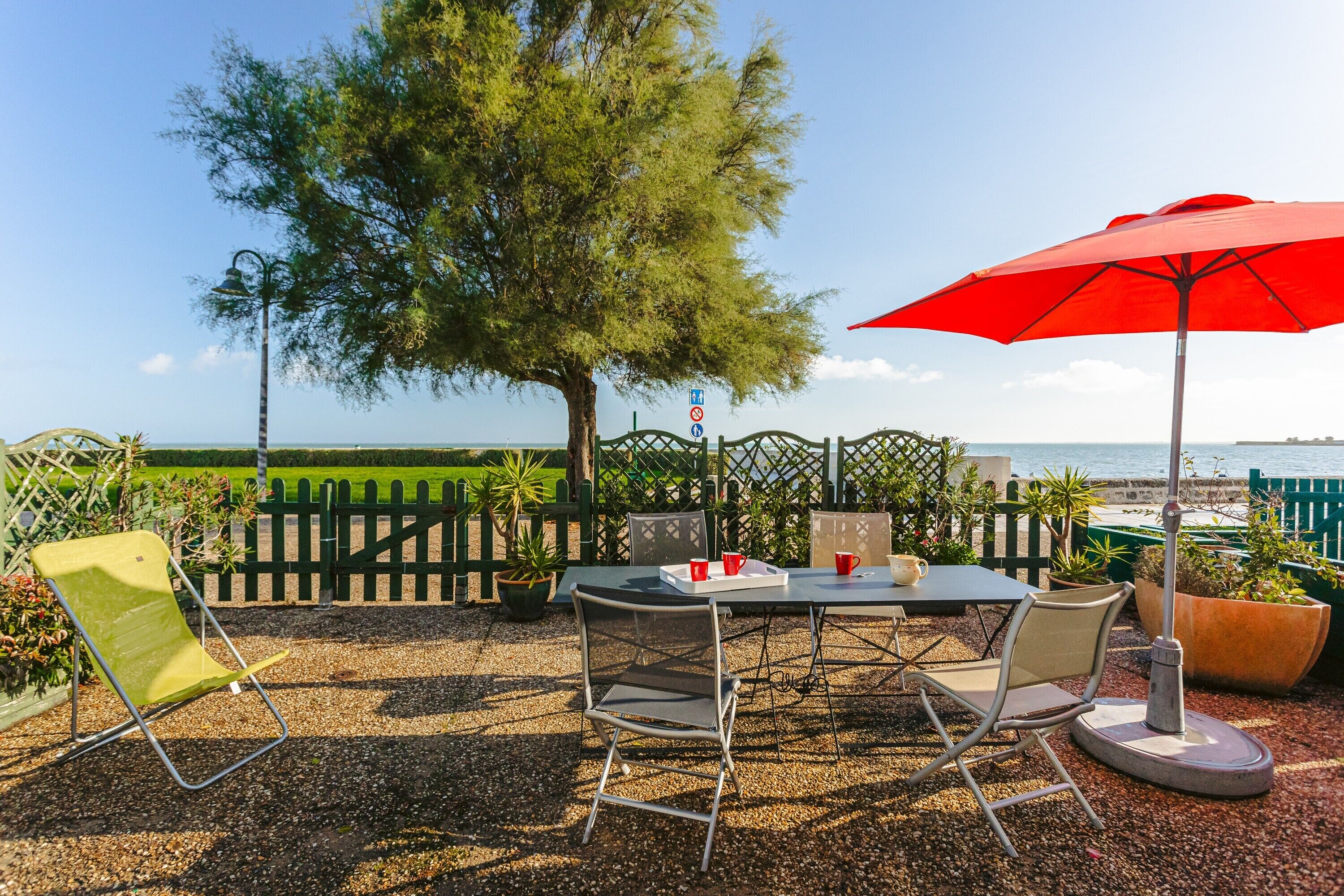 An outdoor patio with a table, chairs, and a red umbrella.