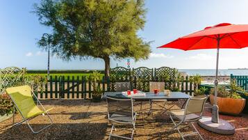 An outdoor patio with a table, chairs, and a red umbrella.