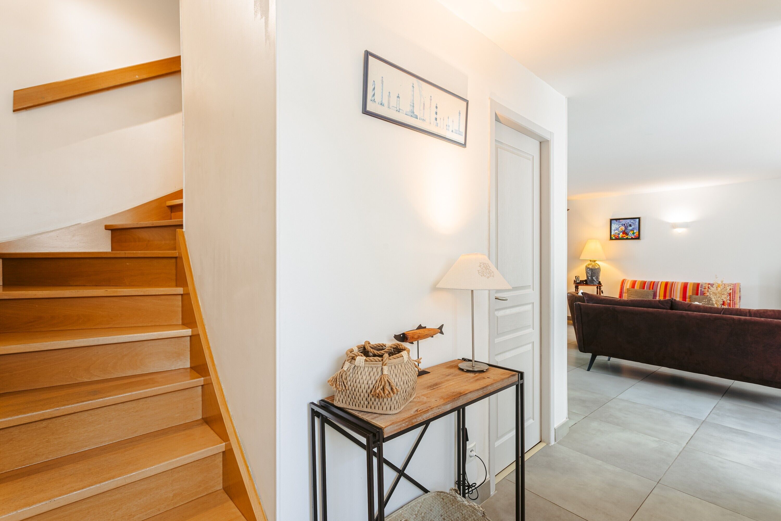Un escalier menant à une pièce dotée d’un plancher en bois, d’une table avec une lampe et d’un canapé à l’arrière-plan.