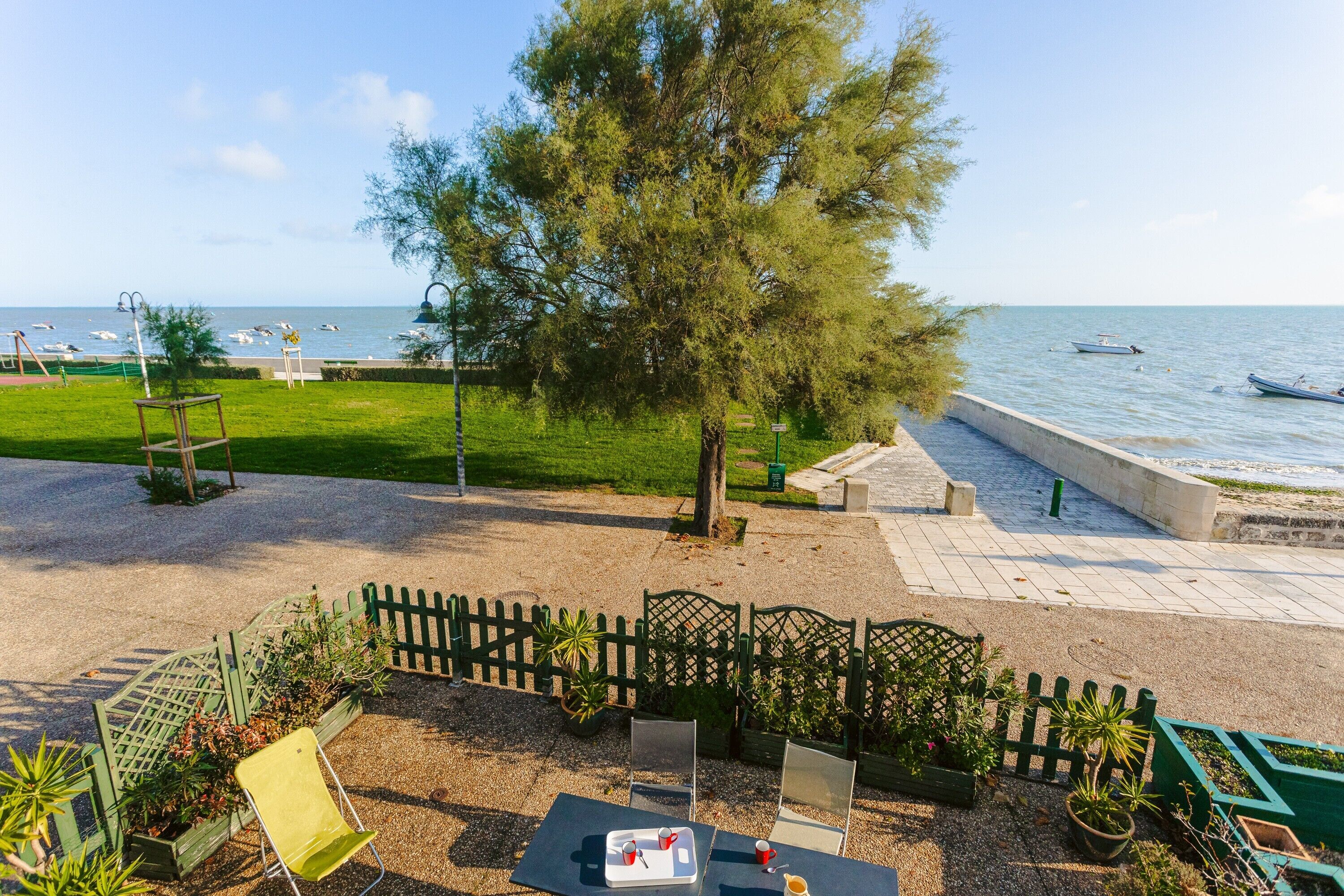 A patio area with a view of the sea, outdoor seating, and a small boat docked nearby.