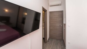 A narrow hallway with a flat-screen TV mounted on the wall, a wooden door, and an air conditioning unit on the wall.