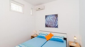 A bedroom with a bed, two bedside tables with lamps, a window, and an air conditioning unit.