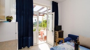 A room with a bed, a TV, a table with wine glasses, and a view of an outdoor patio with a table and chairs.