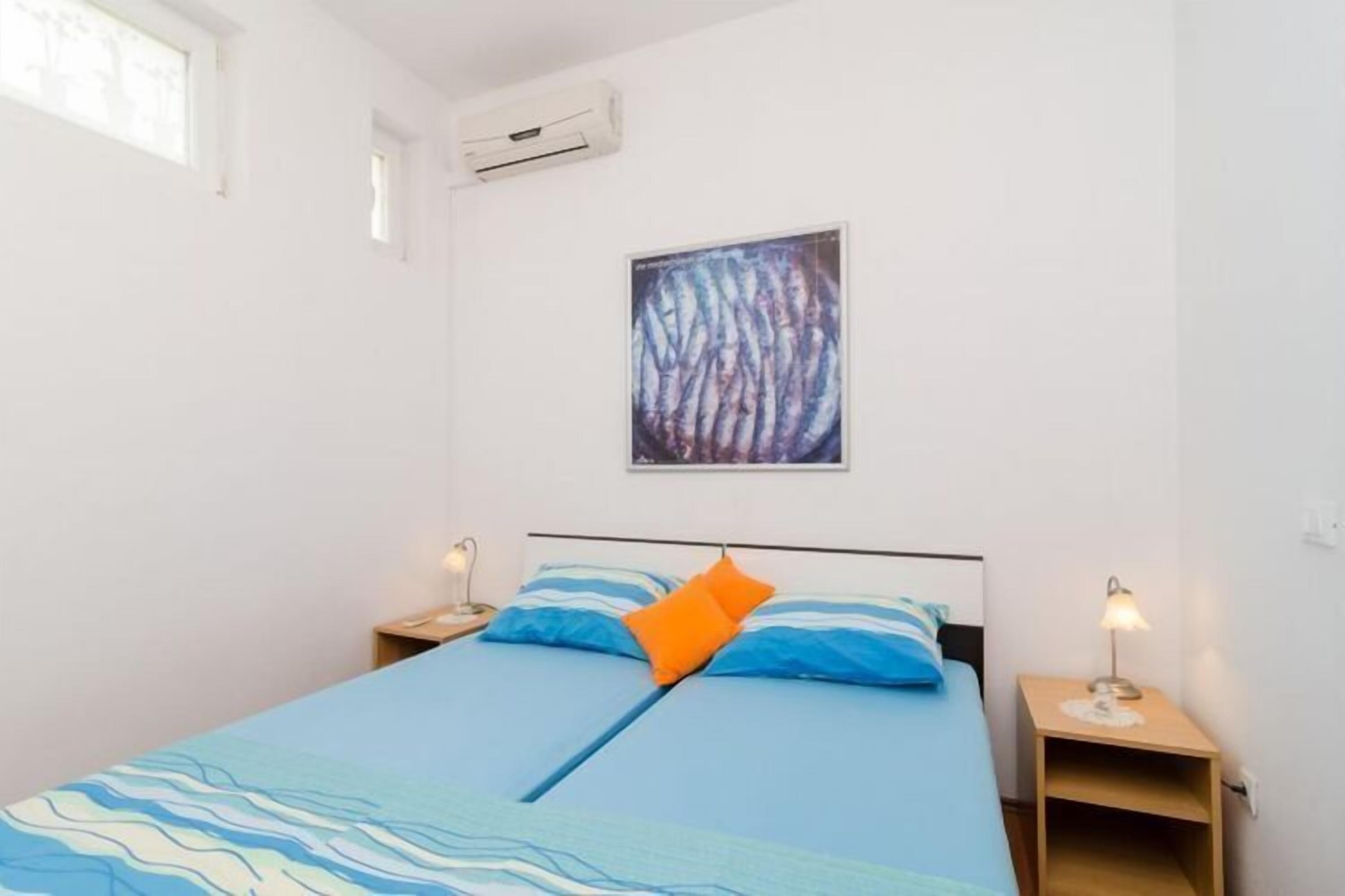 Une chambre à coucher comprenant un lit, deux tables de chevet, un climatiseur fixé au mur et un tableau encadré.