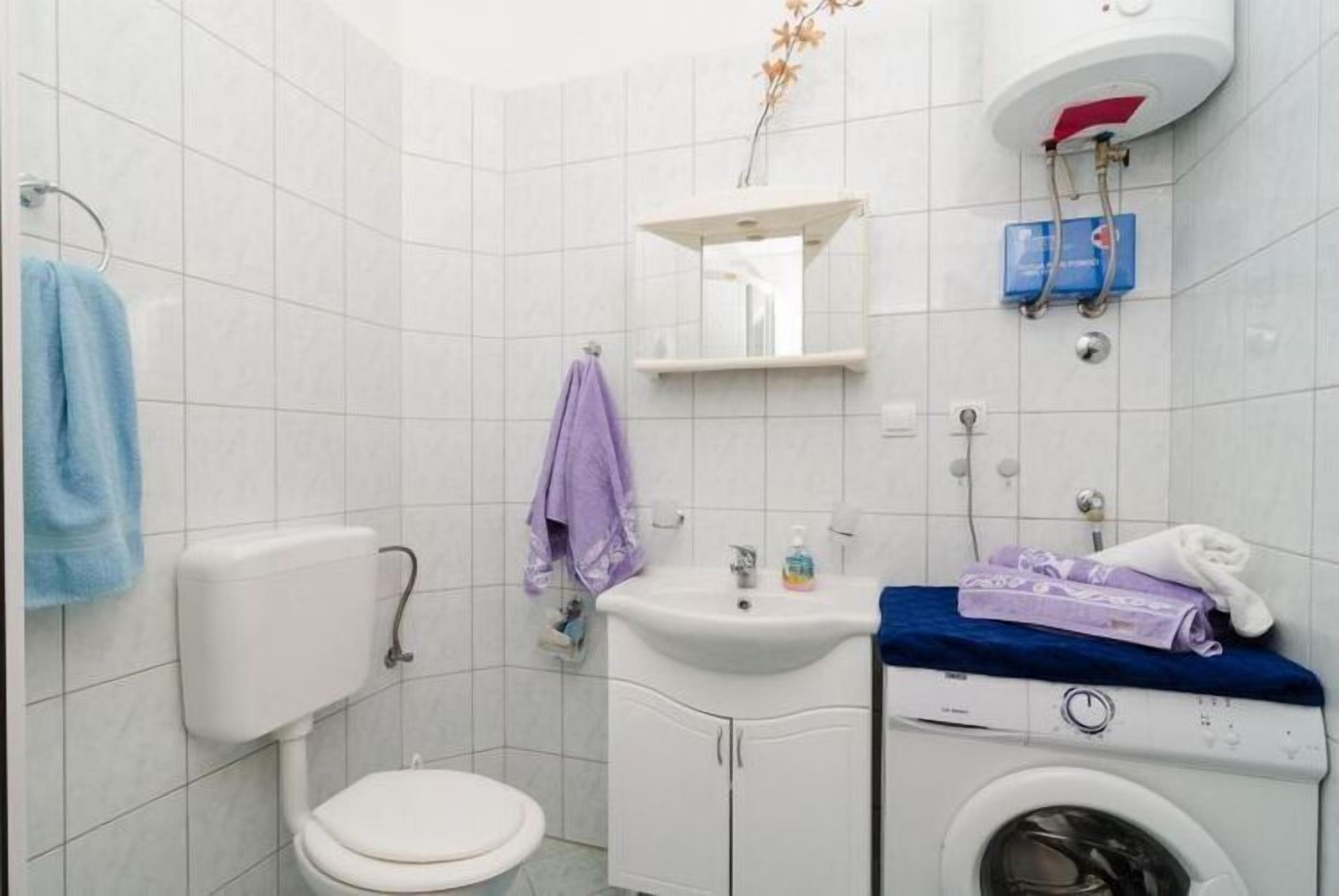 Ett badrum med toalett, handfat, spegel och tvättmaskin.