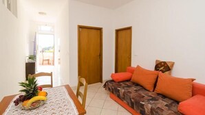 A living room with a sofa, a dining table with a fruit bowl, and two wooden doors. - Apartments Mamma Mia - Comfort One Bedroom Apartment with Terrace (Mlini)