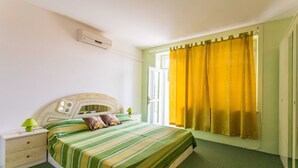 Une chambre à coucher comprenant un lit, une table de chevet, une lampe, une fenêtre avec des rideaux et un appareil de climatisation.