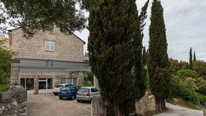 Un bâtiment à la façade en pierre, des voitures garées et de grands cyprès.