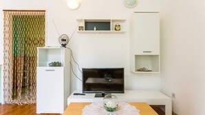 Un salon moderne doté d’un téléviseur à écran plat, de meubles blancs, d’une petite table surmontée d’un vase en verre et d’un rideau décoratif.