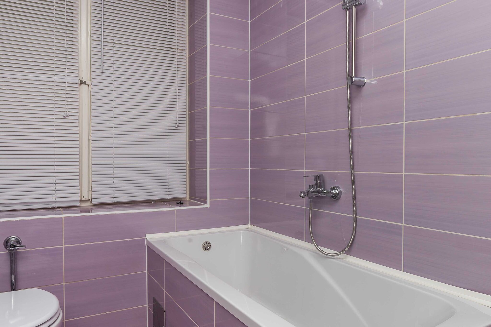 Un bagno con una vasca, un water e una finestra con persiane.