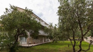 Un bâtiment à deux étages doté d’un balcon, entouré d’arbres et d’une pelouse.
