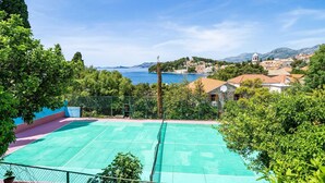 Una cancha de tenis con vistas a un pueblo costero y montañas al fondo.