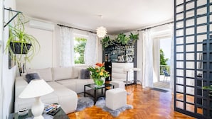 Una sala de estar moderna con un sofá, una mesa de centro y una lámpara. Se observa una estantería llena de libros y objetos decorativos.