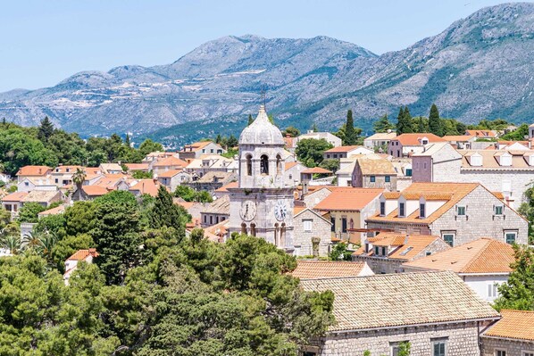 A historic town with stone buildings, a prominent clock tower, and mountains in the background.