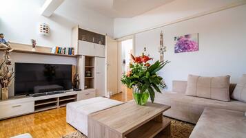 Una sala de estar moderna con una televisión de pantalla plana, una mesa de centro de madera, un sofá color beige y una estantería.