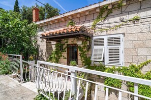 Ein Gebäude aus Stein mit einem Ziegeldach, weißen Fensterläden und einem Balkon mit weißer Brüstung.