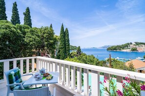 Ein Balkon mit Tee-Gedeck, mit Blick auf eine Küstenlandschaft mit Bäumen und Gebäuden.