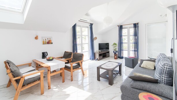Una sala de estar moderna con un sofá, sillas, una mesa de centro, un televisor y un comedor con una mesa y sillas.