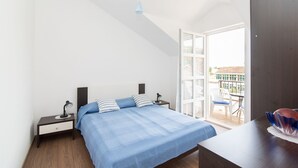 Un dormitorio con cama, mesitas de noche, un escritorio y un balcón con vistas.