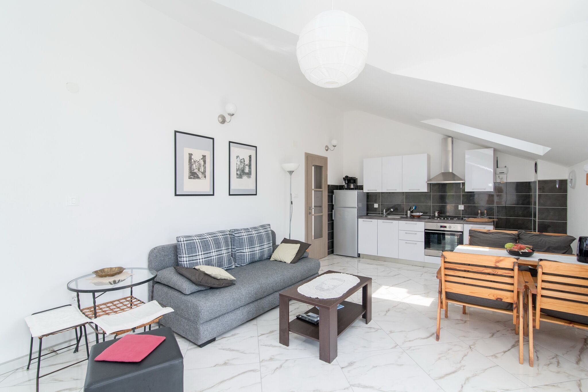Eine moderne Wohnung mit grauem Sofa, einem kleinen runden Tisch, einer Holzbank und einer Küchenzeile mit weißen Schränken und einer schwarzen Arbeitsplatte.