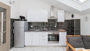 Una cocina moderna con tragaluz, armarios blancos, horno empotrado y una zona de estar con un banco de madera.