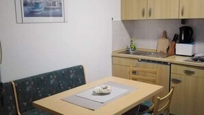 A compact kitchen with wooden cabinets, a sink, and a coffee maker. There is a dining table with a chair and a bench with a cushion. - Apartments Marija - One Bedroom Apartment with Balcony and Sea View (Žuti A2) (Pirovac)