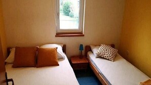 A small, single-room hotel room with two beds, a window, and a nightstand with a lamp. - Apartments Marija - One Bedroom Apartment with Balcony and Sea View (Žuti A2) (Pirovac)